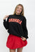 A woman modeling a black long-sleeve sweatshirt with 'GEORGIA' in red block letters outlined in white across the chest, paired with a red mini skirt, against a plain white background.