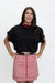 A woman posing in a black short-sleeve top and a red and white vertically striped skirt with a black belt featuring a gold buckle.