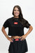 A woman modeling a black short-sleeve crop top and matching black skirt set against a plain white studio background. The outfit features red rectangular logo patches on the chest and waistband with the text 'GO DANCE'.