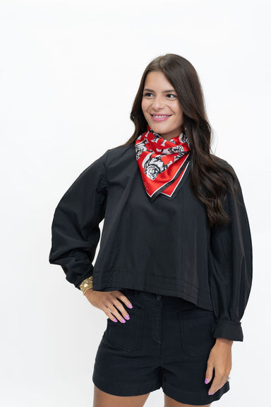 A woman modeling a black cropped long-sleeve top with black shorts and a red patterned bandana around her neck, photographed against a plain white studio background.