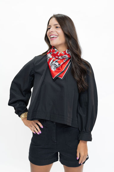 A woman wearing a black cropped bomber jacket, black denim shorts, and a red bandana with a black tiger print around her neck, posing against a solid white background.