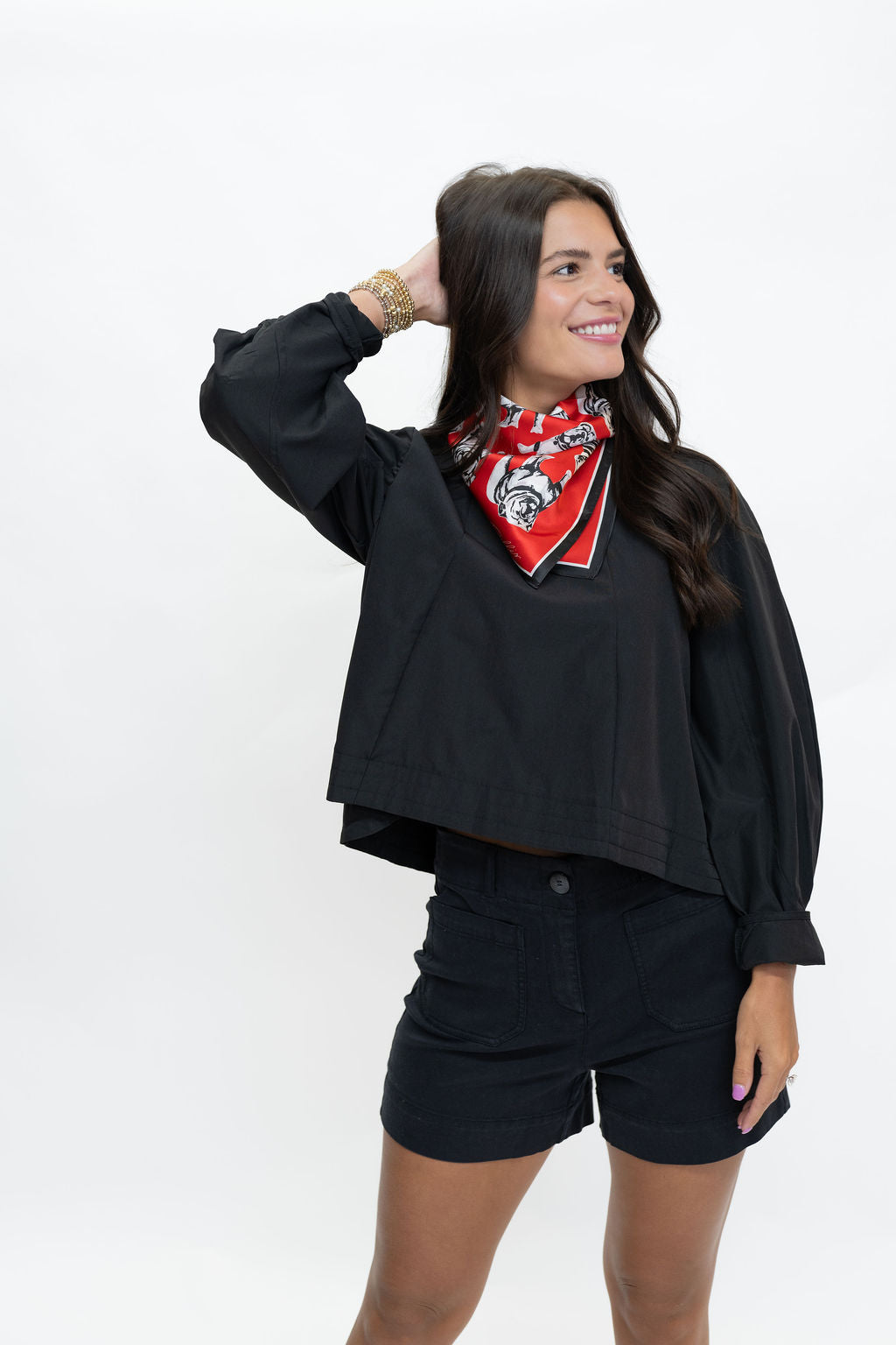 A woman modeling a black cropped long-sleeve top with balloon sleeves, paired with black shorts and a red patterned bandana, against a plain white studio background.