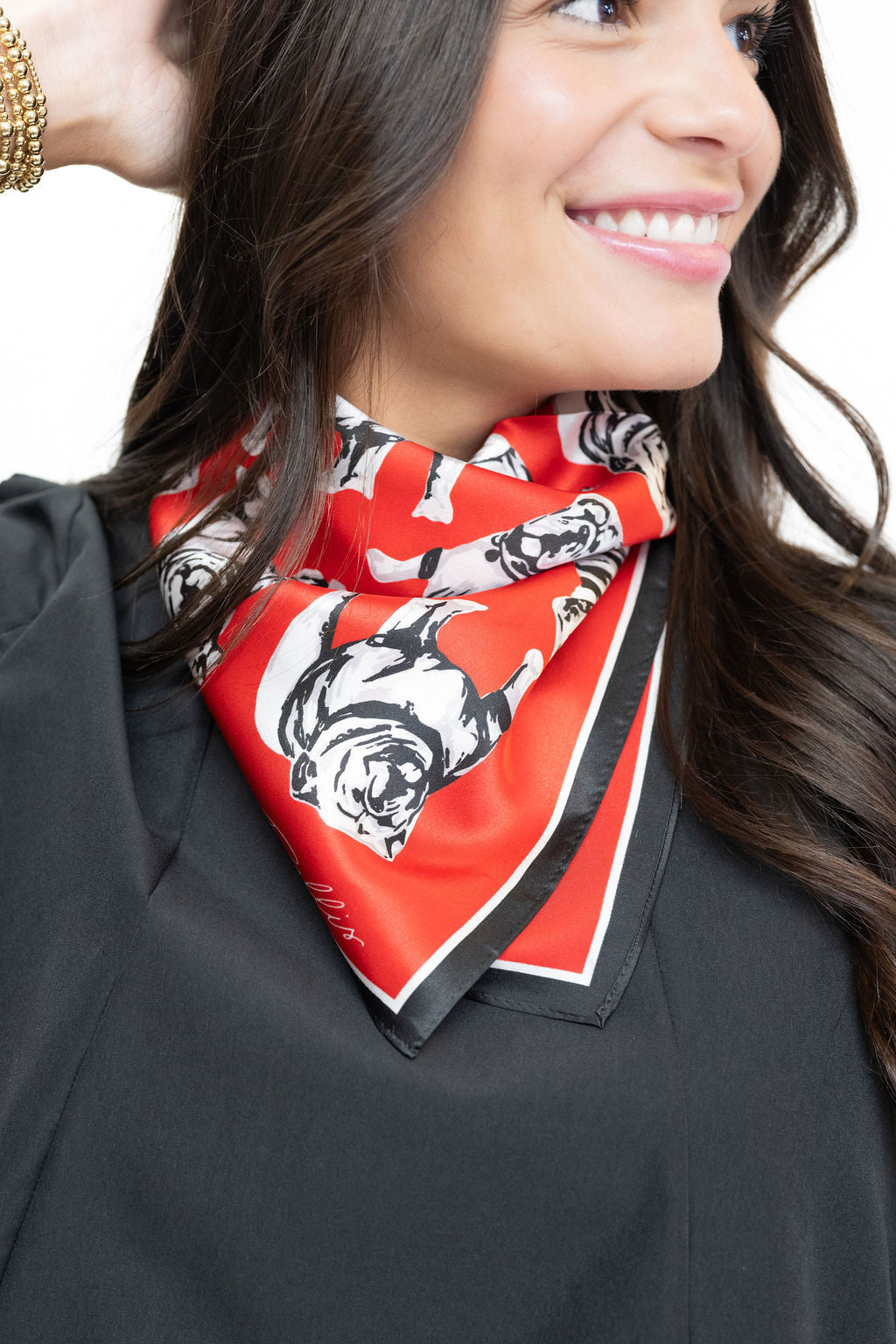 A close-up of a woman wearing a red silk scarf with a black and white graphic print, styled around her neck over a black top.