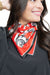 A close-up of a woman wearing a red silk scarf with a black and white graphic print, styled around her neck over a black top.