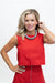 A woman with blonde hair wearing a bright red sleeveless crop top and matching red skirt, accessorized with a chunky silver necklace, posing against a plain white background.