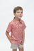 A young boy smiling and looking to the side, wearing a short-sleeve collared polo shirt with a red and white floral pattern, paired with beige shorts, against a plain white background.