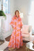Woman wearing a pink dress with orange leaf pattern in a bright living room.