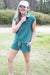 Woman in green outfit with white cap standing outdoors on grass
