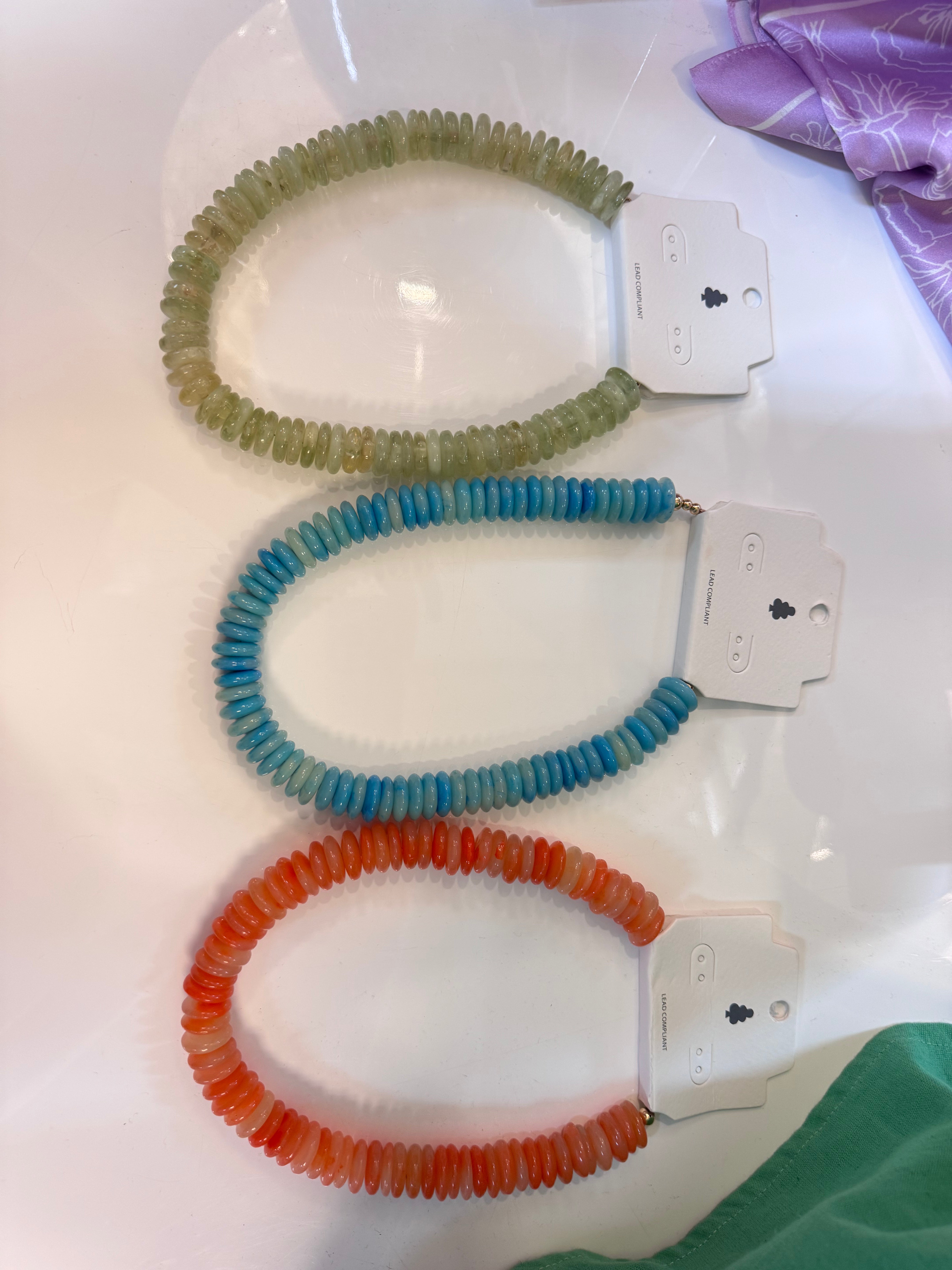 Three beaded necklaces in green, blue, and red on a white surface with tags.