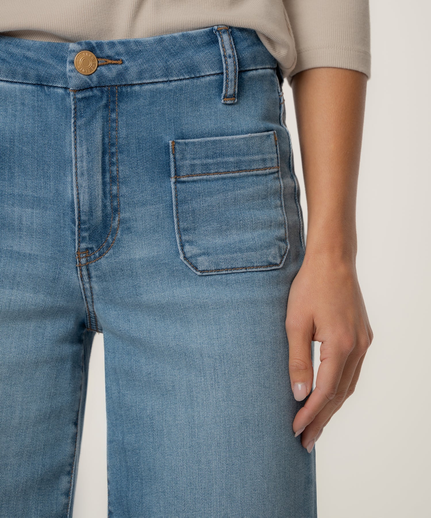Close-up of blue jeans with a hand touching the pocket on a neutral background