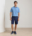 Man wearing a blue polo shirt and navy shorts standing against a plain background