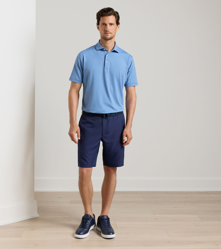 Man wearing a blue polo shirt and navy shorts standing against a plain background