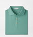 A folded Peter Millar men's polo shirt in a teal green color with a small white geometric pattern, featuring a collar and three buttons, set against a plain white background.