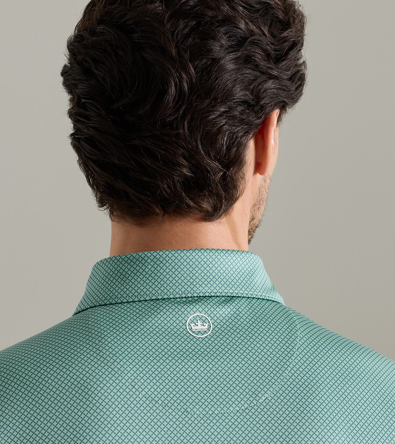 Rear view of a man wearing a mint green patterned collared shirt against a neutral gray background.