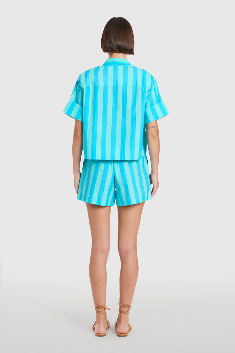 Person wearing a turquoise striped shirt and shorts set on a white background