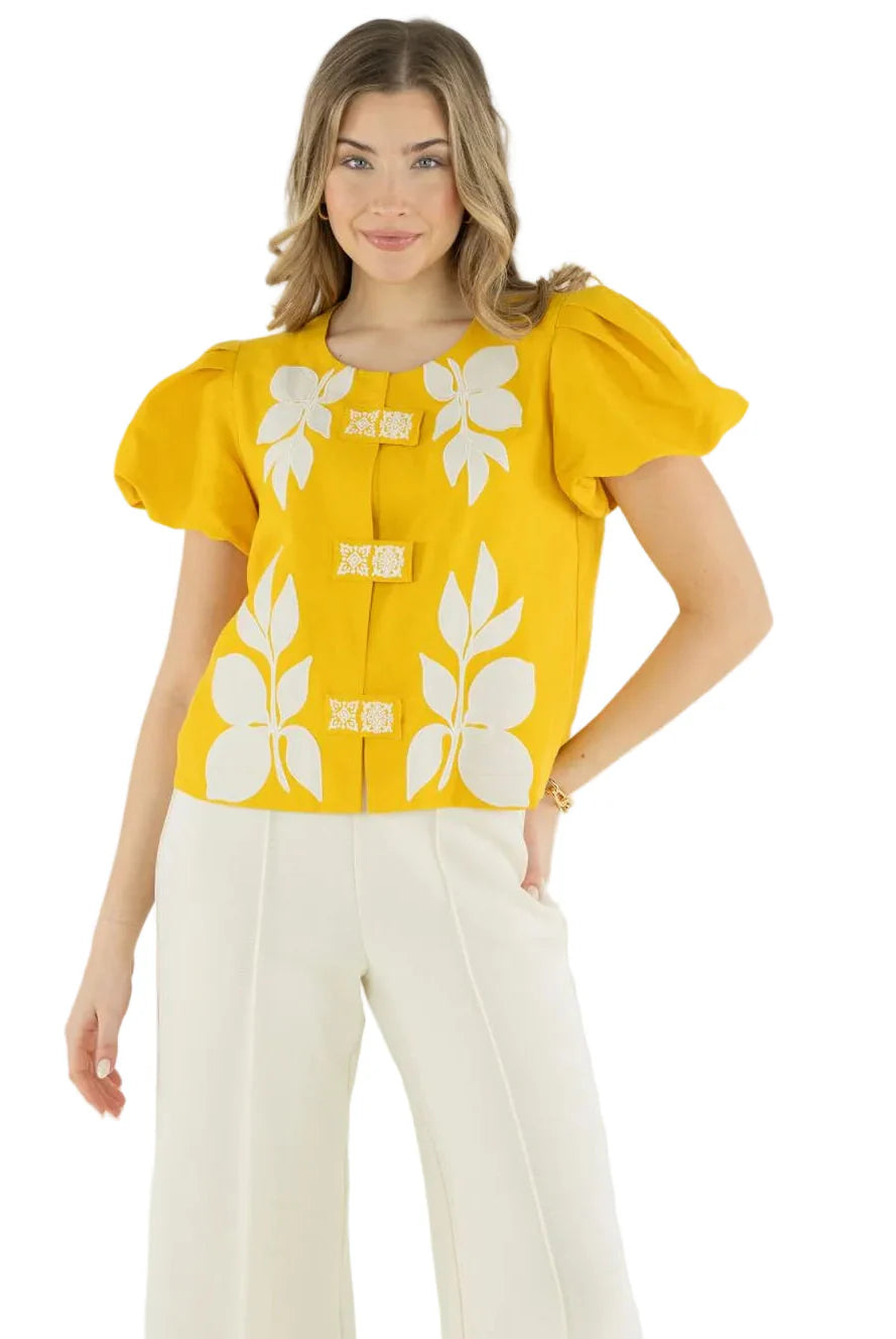Woman wearing a yellow top with white floral patterns on a white background