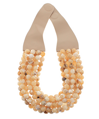 Necklace with beige and white beads on a beige holder against a white background