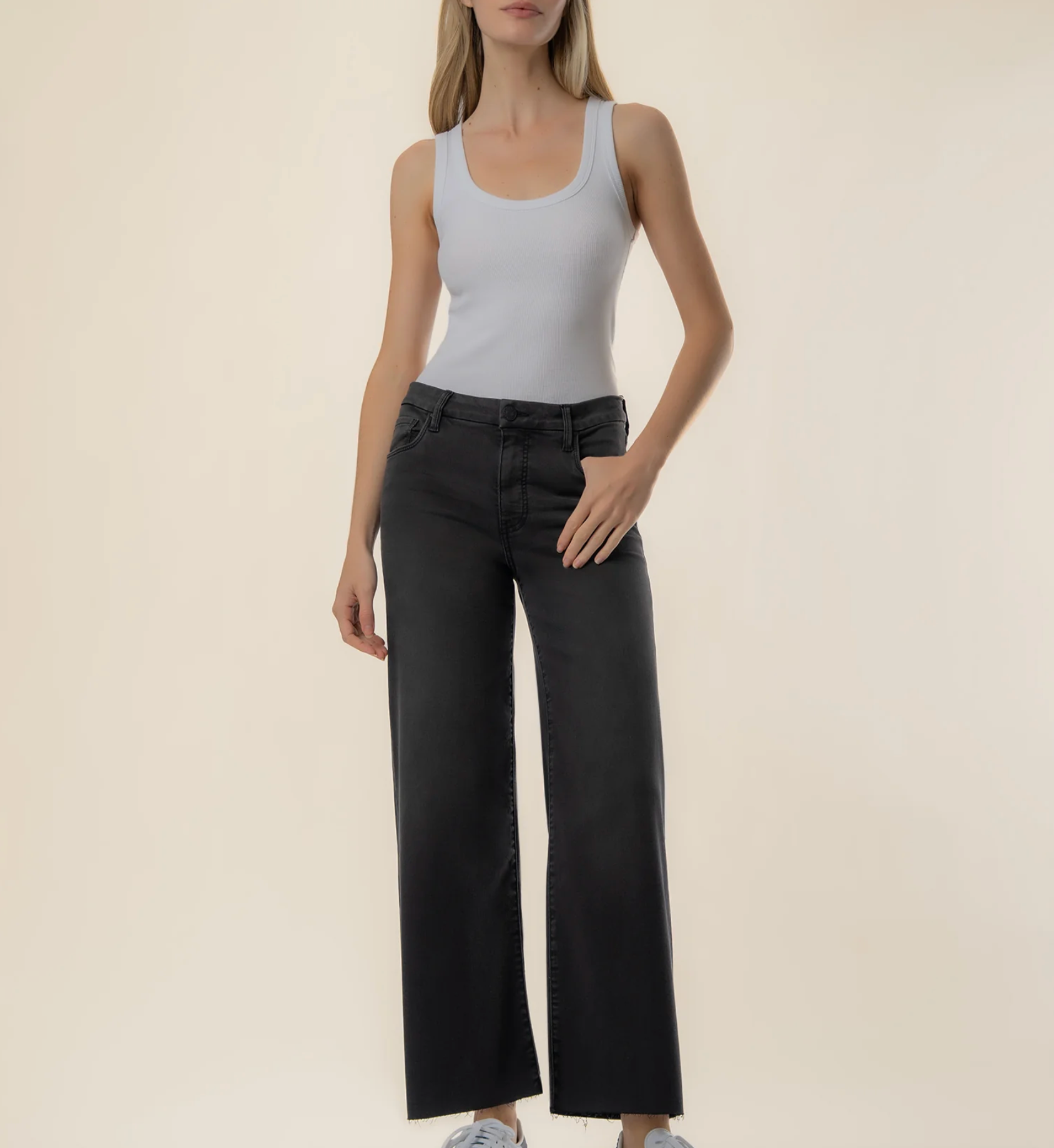 A model wearing a light gray ribbed tank top and black wide-leg jeans, standing against a solid beige studio background.