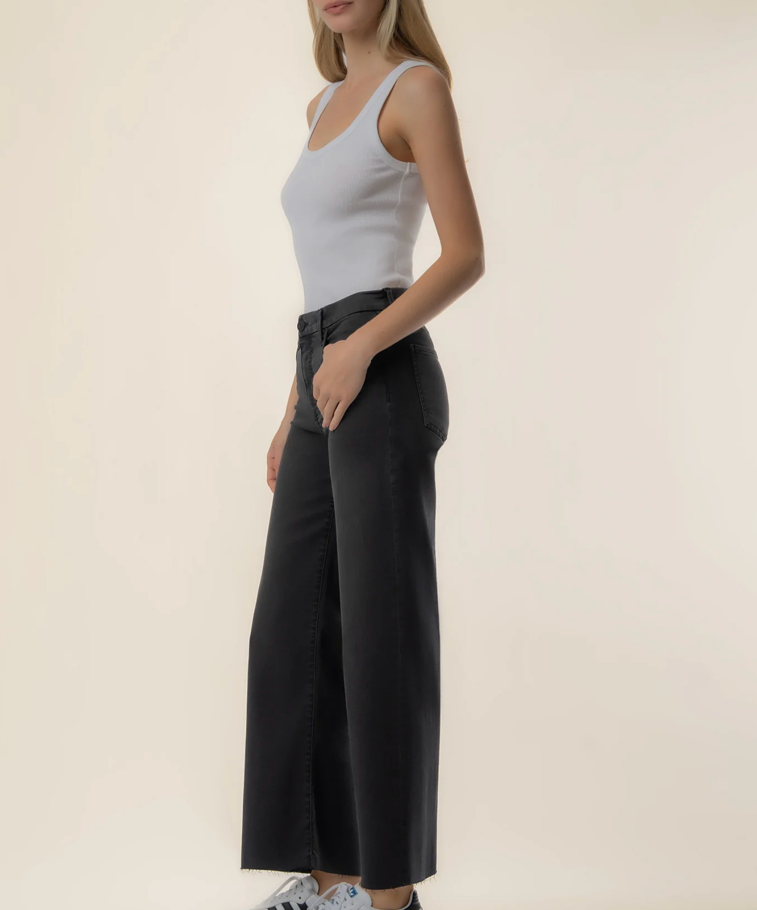 A woman modeling a white ribbed tank top and black wide-leg cropped pants against a plain beige studio background.