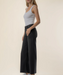 A woman modeling a white ribbed tank top and black wide-leg cropped pants against a plain beige studio background.