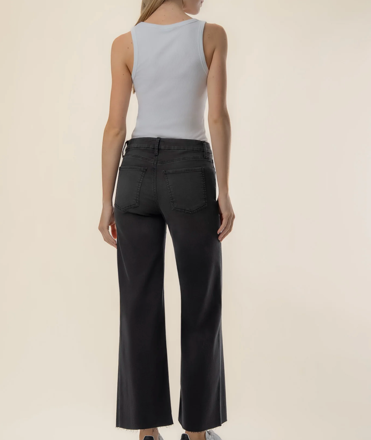 Rear view of a model wearing black wide-leg cropped pants and a light gray sleeveless top against a plain beige studio background.