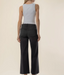 Rear view of a model wearing black wide-leg cropped pants and a light gray sleeveless top against a plain beige studio background.