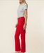 A woman modeling bright red high-waisted flare pants with a white short-sleeve top, shown from the waist down against a plain beige studio background.