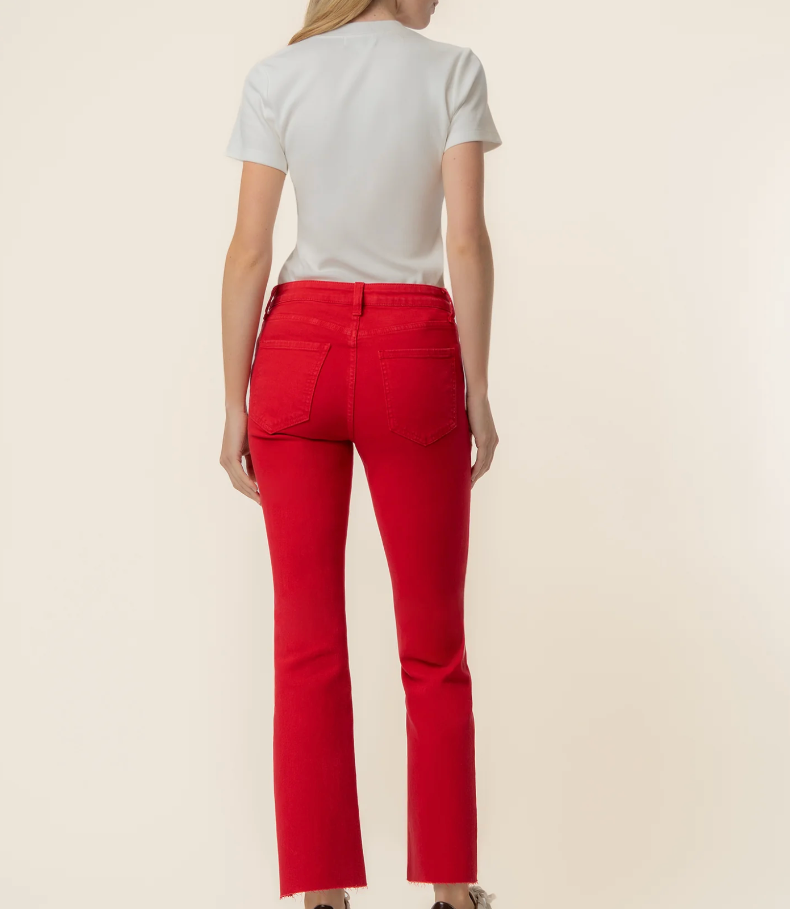 A model shown from the back wearing bright red cropped jeans and a light gray t-shirt, standing against a solid cream background.