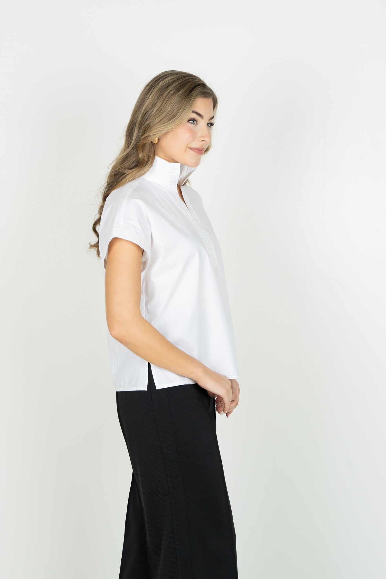 SIDE VIEW OF MODEL WEARING SOLID WHITE V NECK SHORT SLEEVE BLOUSE WITH POPPED COLLAR AND DETAIL ON V NECK