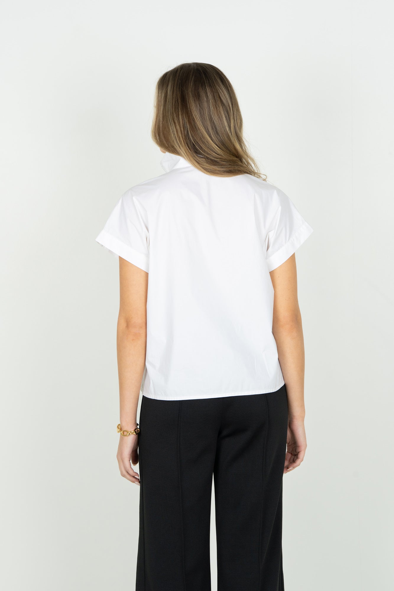 REAR VIEW OF MODEL WEARING SOLID WHITE V NECK SHORT SLEEVE BLOUSE WITH POPPED COLLAR AND DETAIL ON V NECK