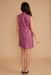 A woman shown from the back wearing a sleeveless, high-neck, knee-length magenta dress with a satin-like sheen, set against a solid beige studio background.