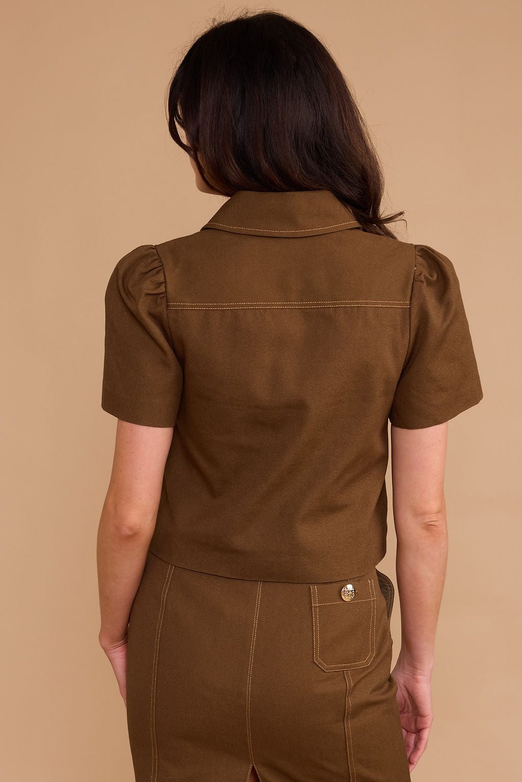Person wearing a brown jumpsuit against a beige background
