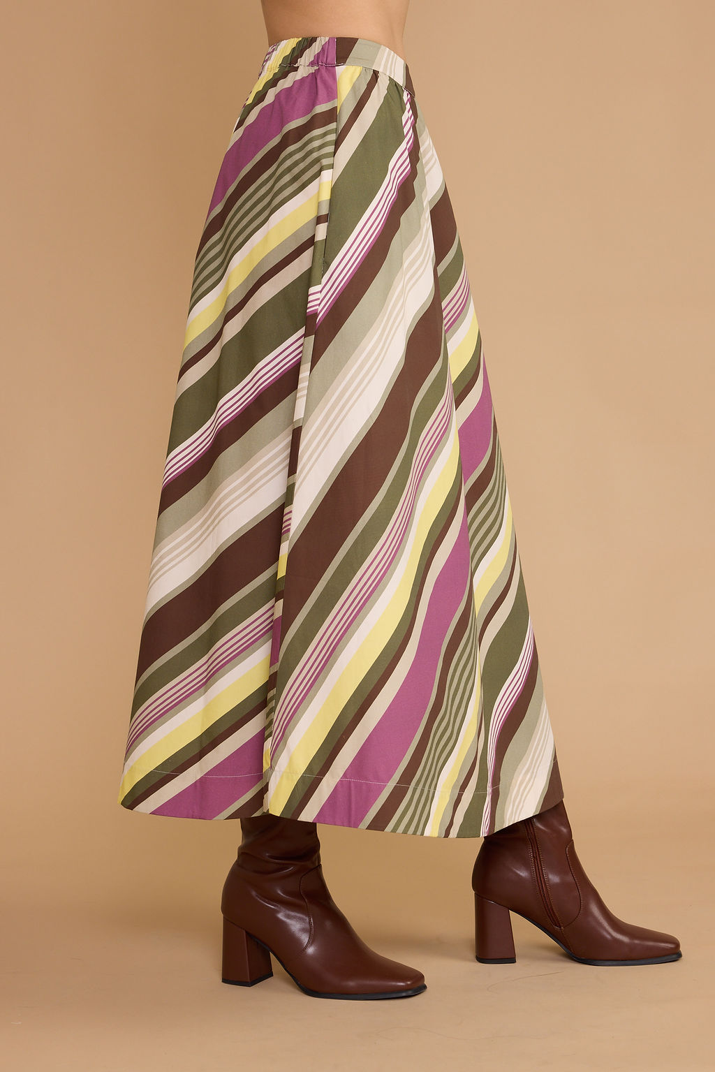 A high-waisted, wide-leg skirt with diagonal stripes in olive green, brown, magenta, yellow, and cream, styled with dark brown heeled ankle boots against a solid beige background.