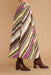 A high-waisted, wide-leg skirt with diagonal stripes in olive green, brown, magenta, yellow, and cream, styled with dark brown heeled ankle boots against a solid beige background.