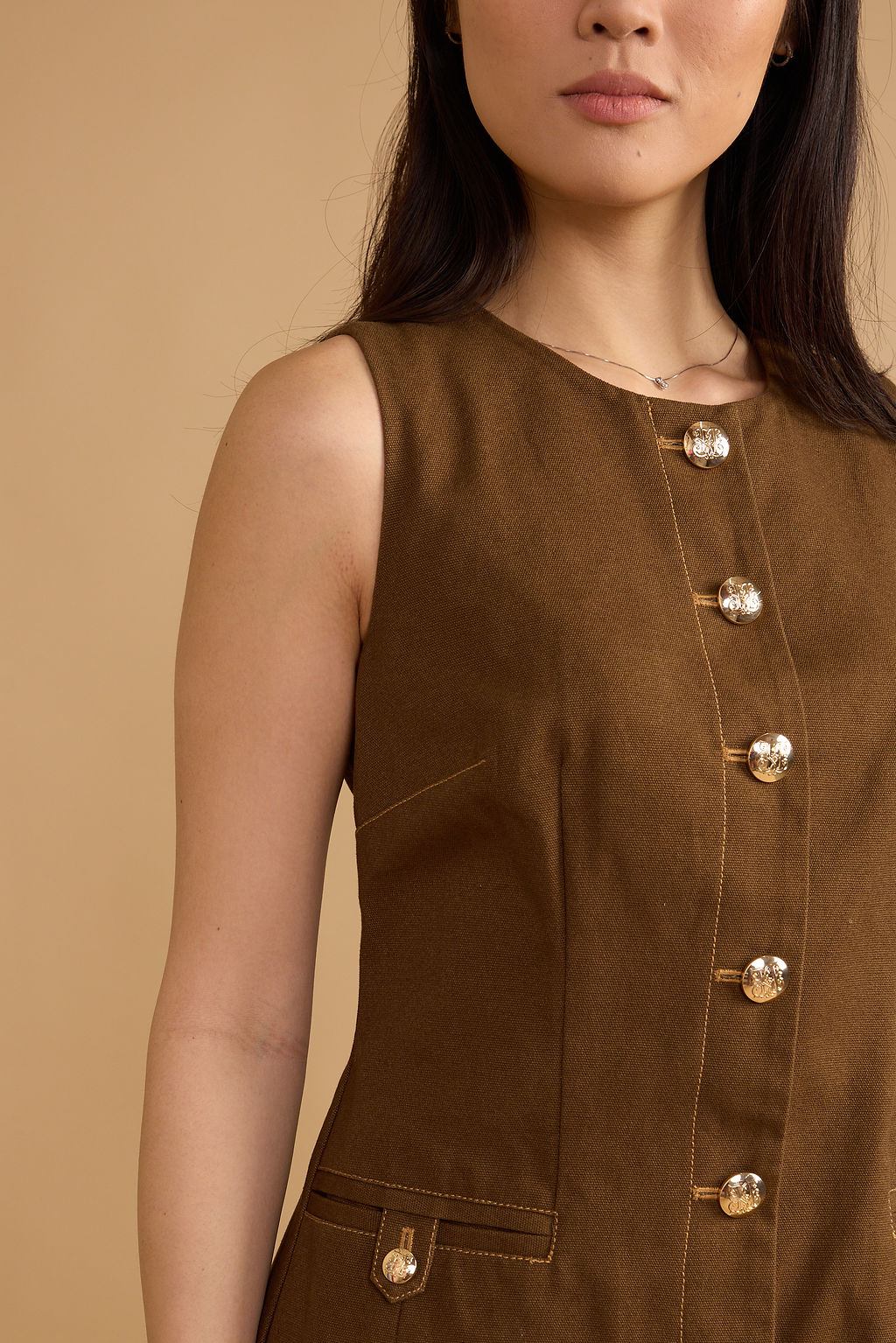 Brown sleeveless top with button details on a beige background