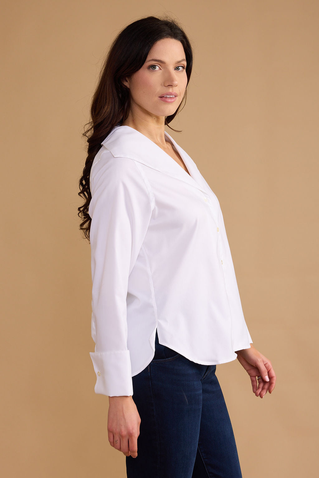 Woman wearing a white blouse and dark jeans against a beige background