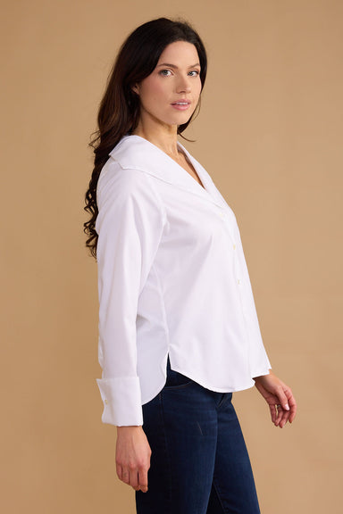 Woman wearing a white blouse and dark jeans against a beige background