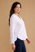 Woman wearing a white blouse and dark jeans against a beige background
