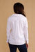 A woman viewed from the back wearing a white long-sleeve button-up shirt and dark blue jeans, standing against a solid beige background.