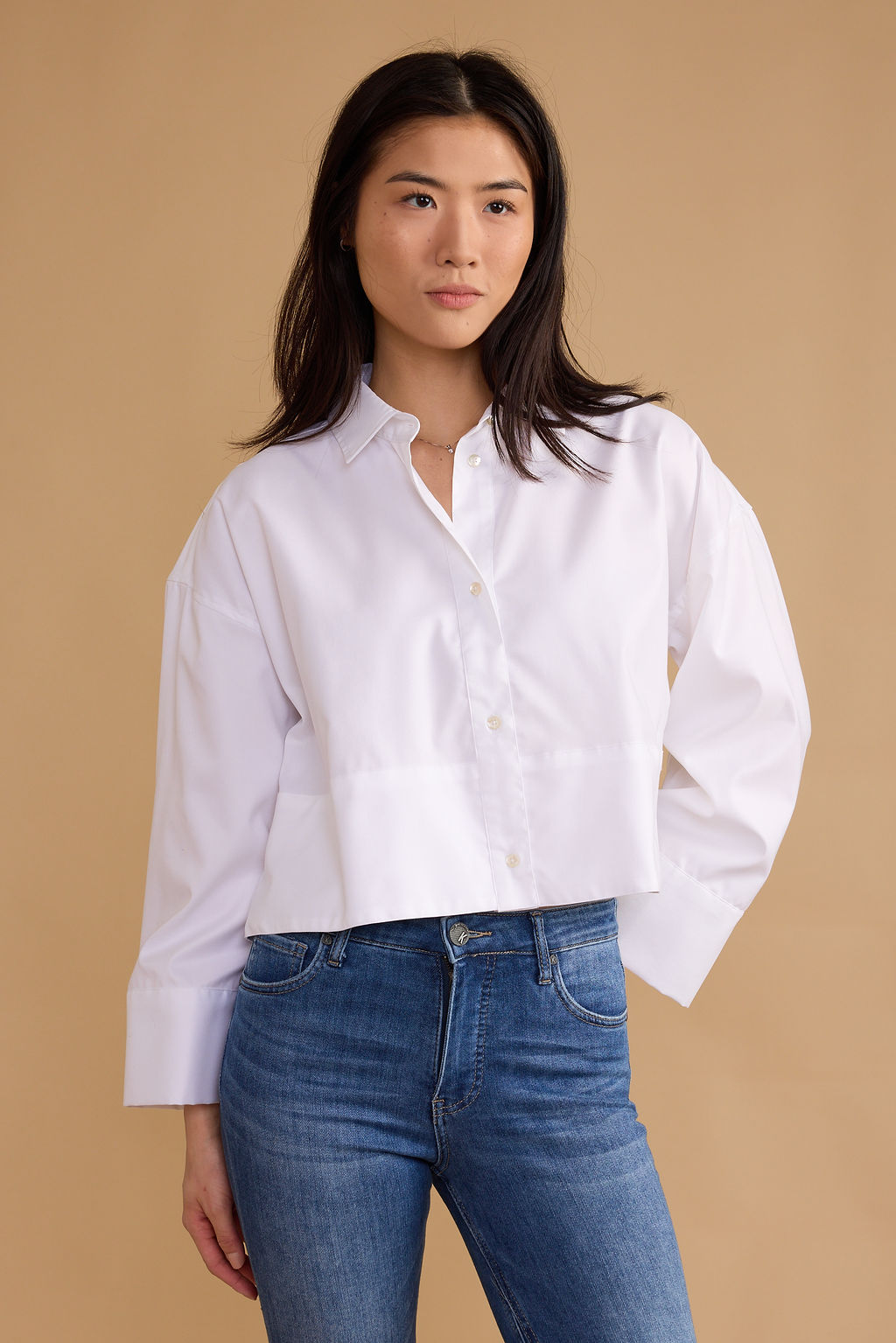 Woman wearing a white shirt and blue jeans against a beige background