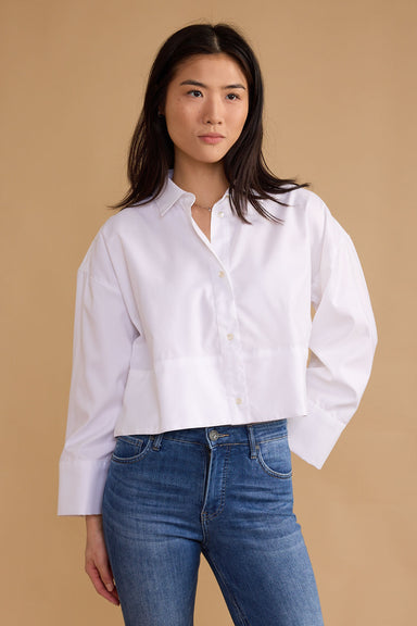 Woman wearing a white shirt and blue jeans against a beige background