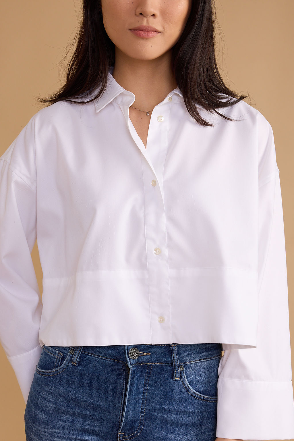 Person wearing a white button-up shirt and blue jeans against a beige background