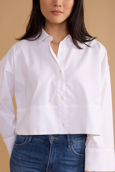Person wearing a white button-up shirt and blue jeans against a beige background