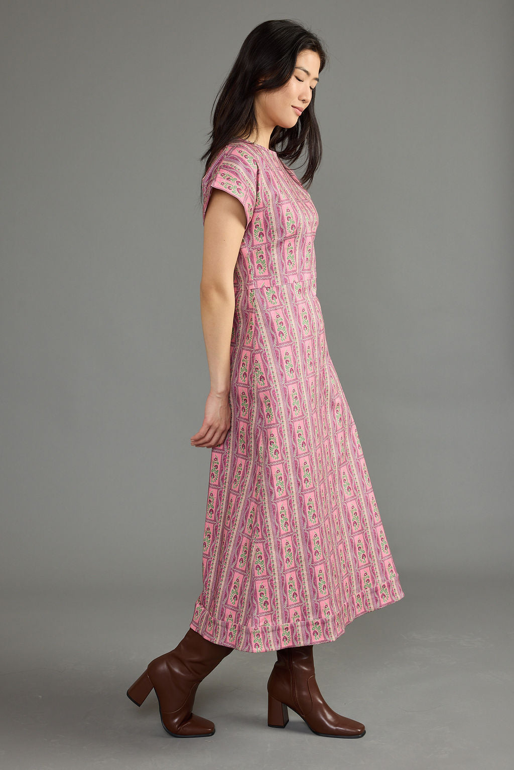 A woman modeling a pink and white patterned midi dress with short sleeves, shown in profile against a solid gray studio background.