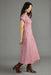 A woman modeling a pink and white patterned midi dress with short sleeves, shown in profile against a solid gray studio background.