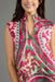 A close-up of a woman wearing a sleeveless high-neck top with a vibrant pink, green, and beige botanical print against a solid gray background.