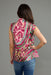 A woman shown from the back wearing a sleeveless peplum-style top with a vibrant pink, green, and beige floral paisley pattern, paired with blue jeans, against a solid gray studio background.