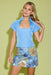 A woman modeling a light blue short-sleeve top with a square neckline and a matching blue floral mini skirt, posed against a solid light green studio background.