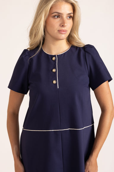 Woman wearing a navy blue dress with white trim on a beige background